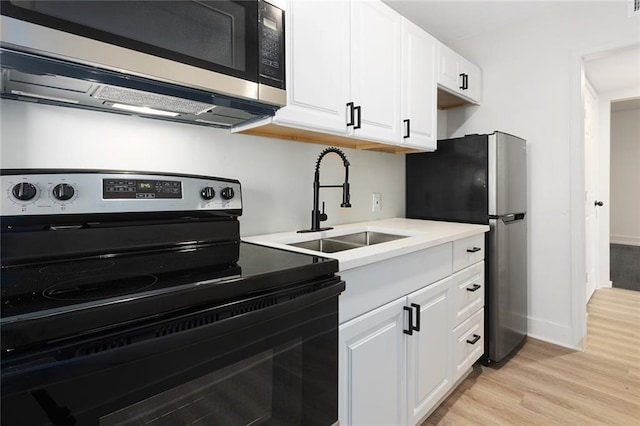 kitchen with a sink, light wood-style floors, white cabinets, light countertops, and appliances with stainless steel finishes