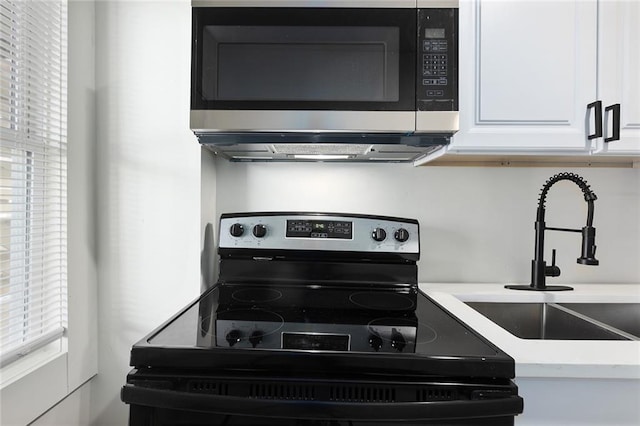 kitchen featuring range with electric cooktop, white cabinets, stainless steel microwave, light countertops, and a sink