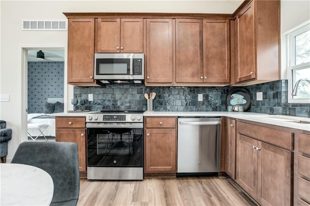 4413 E 135th St, Grandview, MO 64030 - kitchen featuring appliances with stainless steel finishes, a sink, light countertops, decorative backsplash, and light wood-type flooring