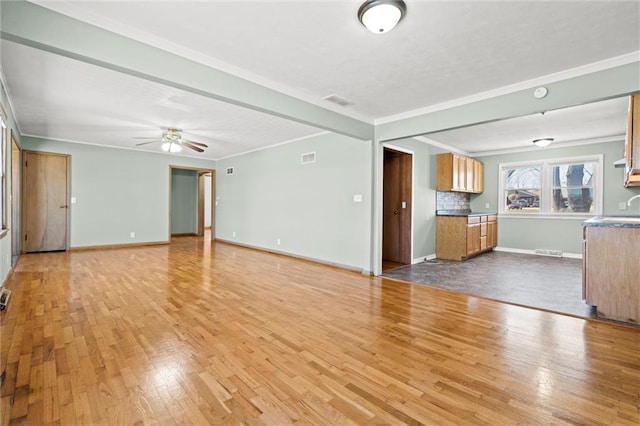 unfurnished living room featuring visible vents, ornamental molding, a ceiling fan, wood finished floors, and baseboards