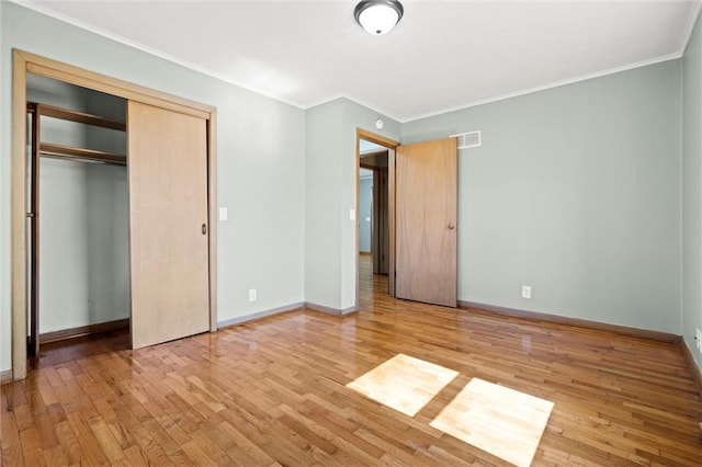 unfurnished bedroom with visible vents, crown molding, baseboards, light wood-type flooring, and a closet