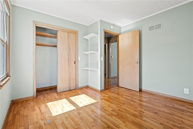 unfurnished bedroom with wood finished floors, visible vents, baseboards, a closet, and crown molding