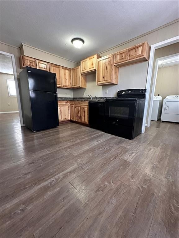 kitchen featuring dark wood finished floors, dark countertops, black appliances, washer and dryer, and baseboards