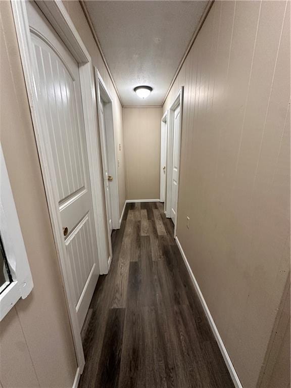 hallway featuring a textured ceiling, baseboards, and dark wood-style flooring