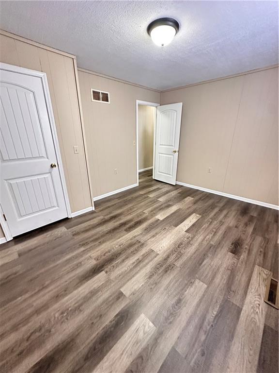 unfurnished bedroom with a textured ceiling, wood finished floors, visible vents, and baseboards