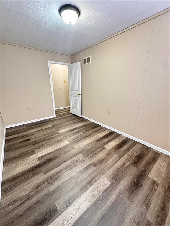 unfurnished room featuring visible vents, a textured ceiling, baseboards, and wood finished floors