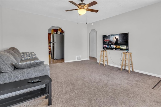 carpeted living area featuring visible vents, arched walkways, baseboards, and ceiling fan