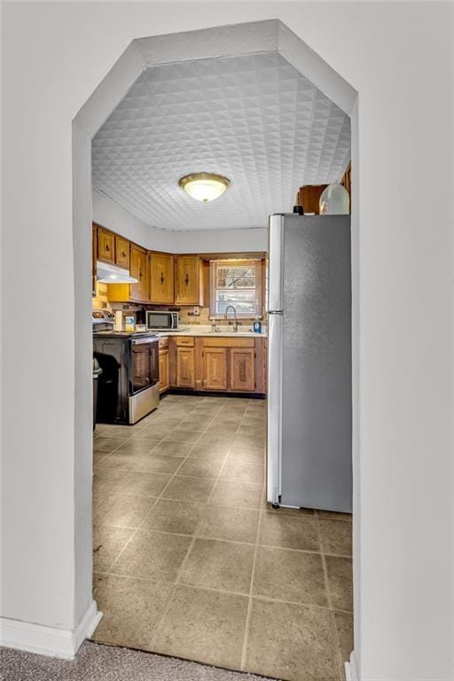 kitchen with under cabinet range hood, light countertops, brown cabinets, stainless steel appliances, and a sink