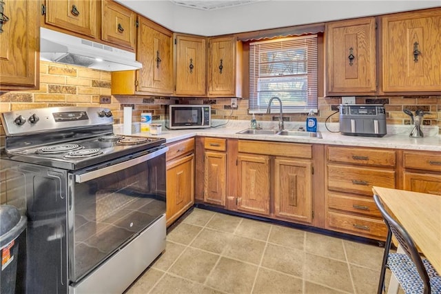 kitchen featuring brown cabinetry, a sink, stainless steel appliances, light countertops, and under cabinet range hood