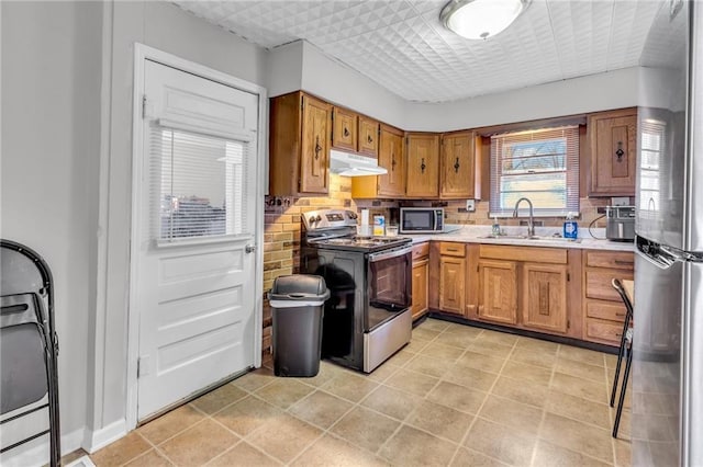 kitchen featuring brown cabinetry, a sink, stainless steel appliances, light countertops, and under cabinet range hood