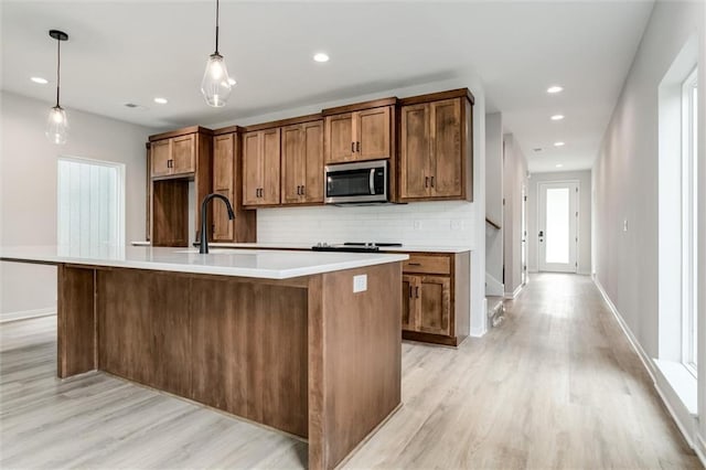 3322 Tracy Ave, Kansas City, MO 64109 - kitchen with stainless steel microwave, light wood finished floors, decorative backsplash, an island with sink, and recessed lighting