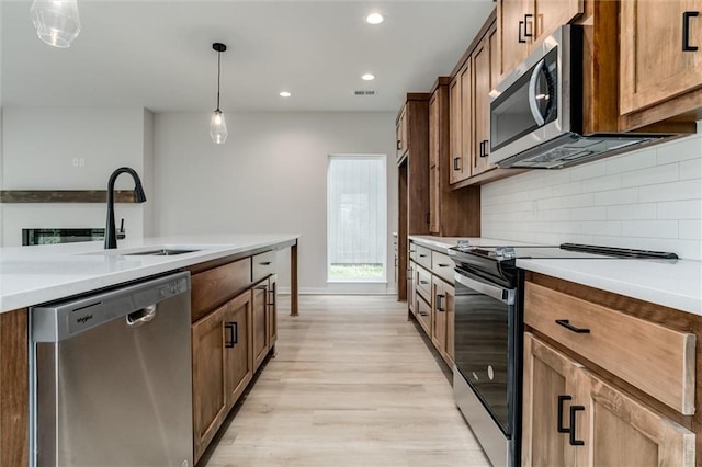 3322 Tracy Ave, Kansas City, MO 64109 - kitchen featuring stainless steel appliances, light wood finished floors, decorative backsplash, a sink, and pendant lighting