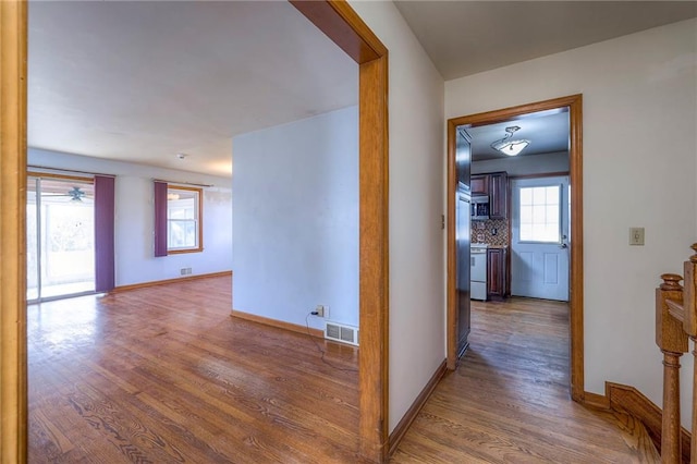 hall with visible vents, baseboards, and wood finished floors