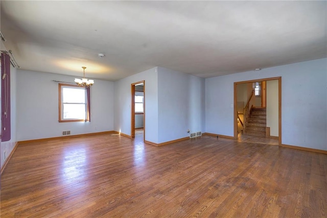 spare room with visible vents, wood finished floors, stairs, and a chandelier