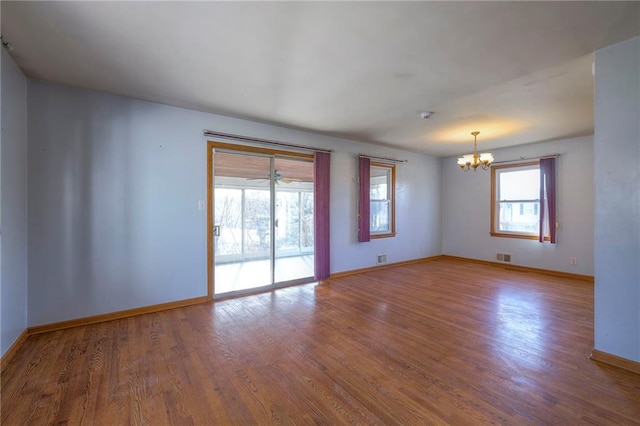 spare room featuring visible vents, a notable chandelier, wood finished floors, and baseboards