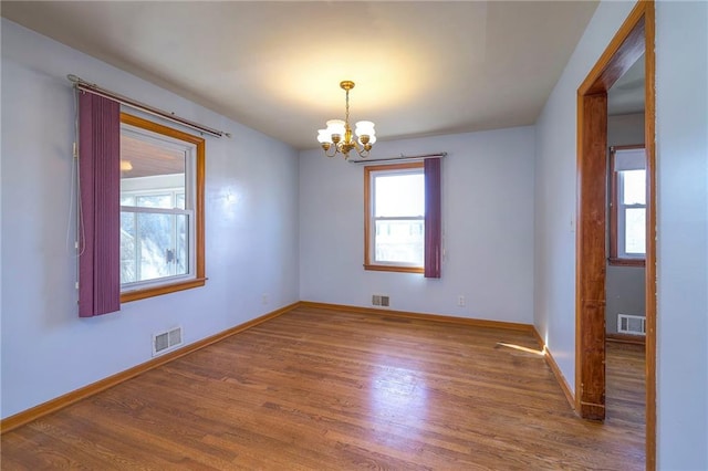 empty room with plenty of natural light, wood finished floors, and visible vents