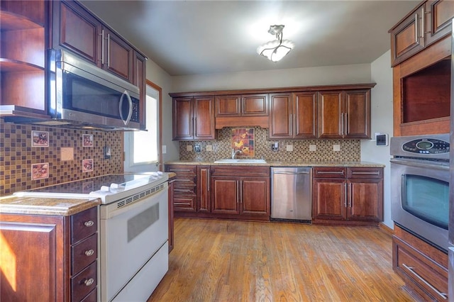 kitchen featuring light wood finished floors, tasteful backsplash, appliances with stainless steel finishes, and a sink