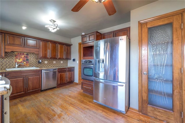 kitchen with light wood finished floors, ceiling fan, a sink, appliances with stainless steel finishes, and backsplash