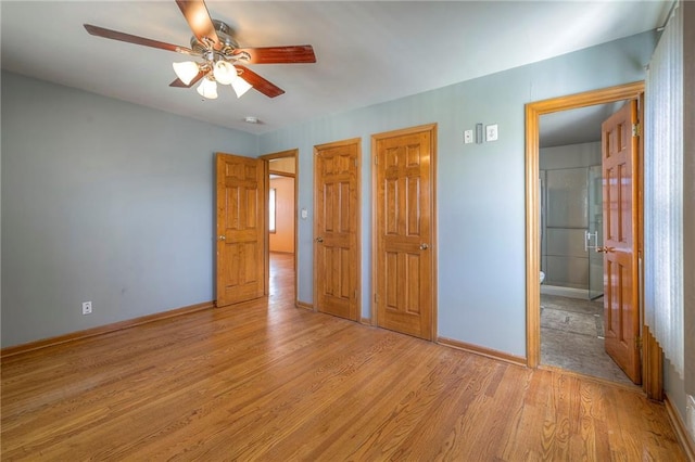 unfurnished bedroom with a ceiling fan, baseboards, light wood-style flooring, ensuite bathroom, and two closets