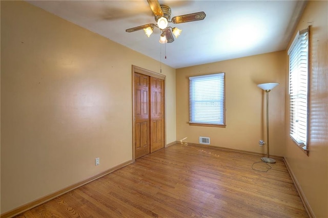 unfurnished room with visible vents, light wood-style flooring, a ceiling fan, and baseboards