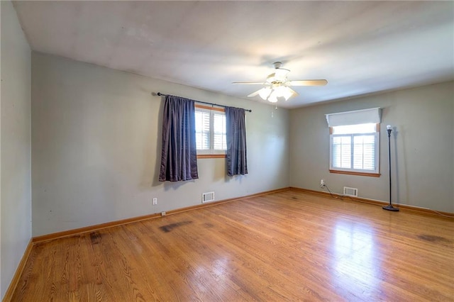 empty room featuring a ceiling fan, wood finished floors, visible vents, and baseboards