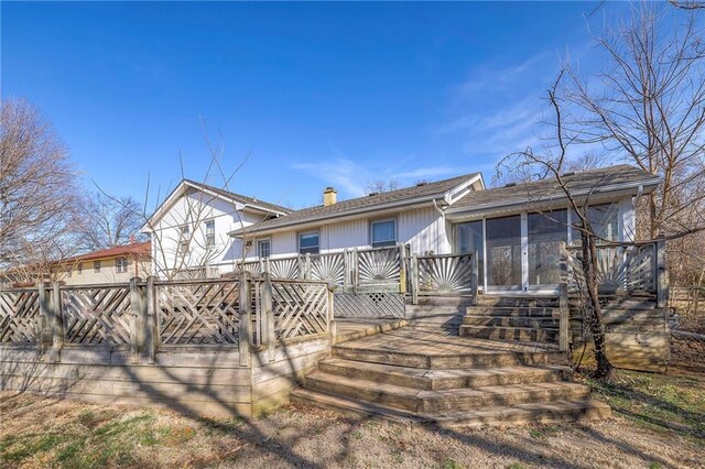 rear view of property featuring a chimney, fence, a deck, and a sunroom