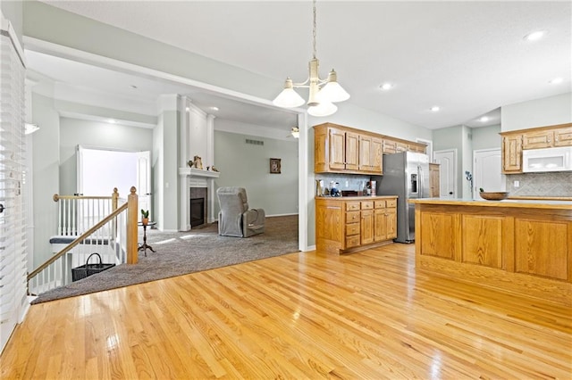 kitchen with decorative backsplash, white microwave, light wood-style floors, a glass covered fireplace, and stainless steel fridge with ice dispenser