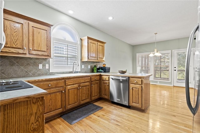 kitchen featuring brown cabinetry, dishwasher, a peninsula, black electric stovetop, and a sink