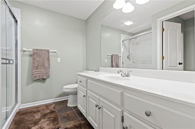 full bathroom with vanity, a shower stall, toilet, and baseboards