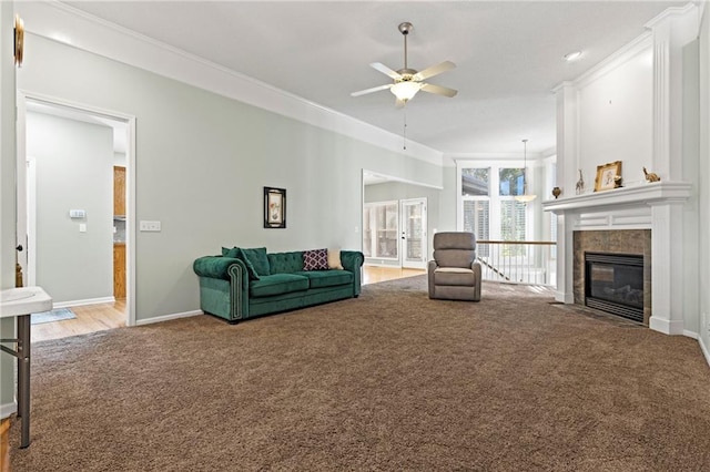 living area featuring crown molding, a ceiling fan, light carpet, a tile fireplace, and baseboards