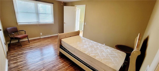 bedroom featuring a baseboard heating unit, wood finished floors, and baseboards