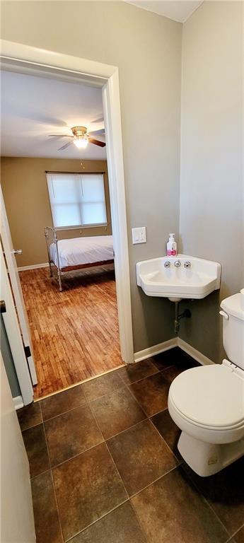 half bath featuring connected bathroom, toilet, a ceiling fan, baseboards, and tile patterned floors