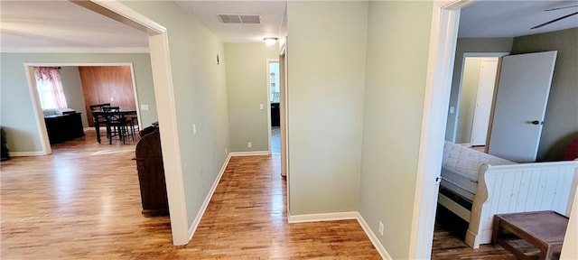 corridor with light wood finished floors, baseboards, and visible vents