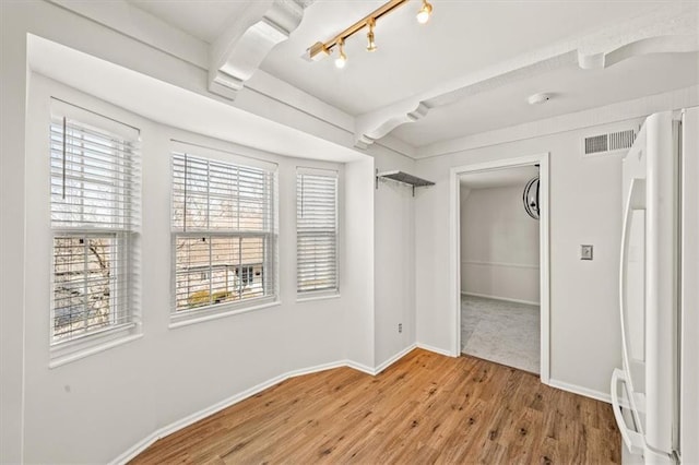 unfurnished room featuring track lighting, wood finished floors, visible vents, and baseboards