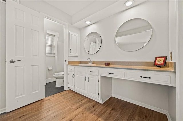 bathroom with vanity, toilet, wood finished floors, and baseboards