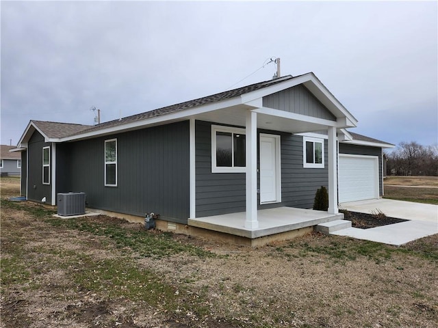 rear view of property featuring driveway, central AC unit, and an attached garage