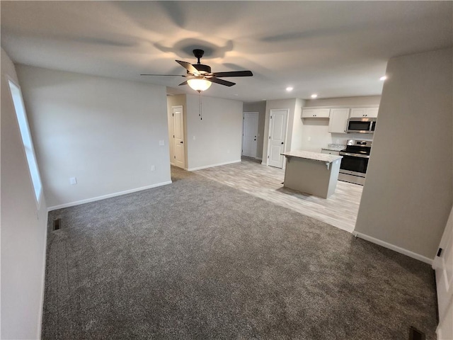 kitchen with light carpet, stainless steel appliances, white cabinetry, and baseboards