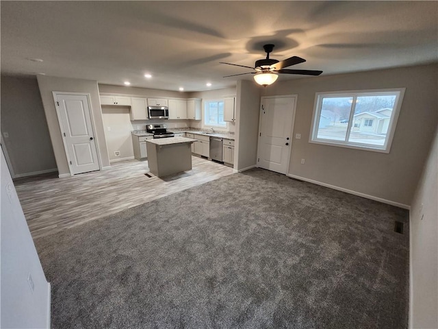 kitchen with light carpet, appliances with stainless steel finishes, open floor plan, and a kitchen island