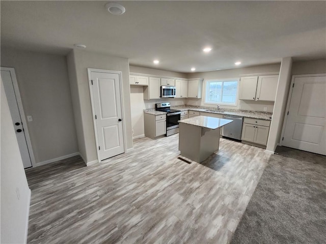 kitchen featuring light wood-style flooring, appliances with stainless steel finishes, a sink, a kitchen island, and baseboards