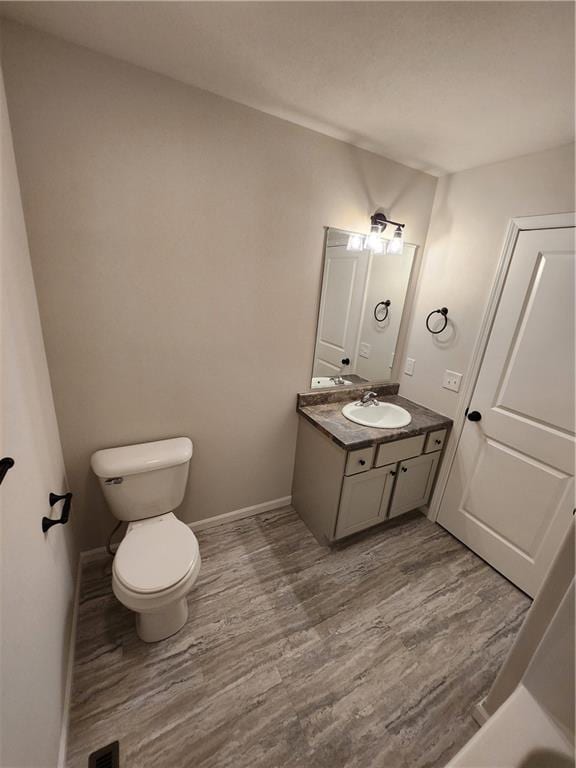 bathroom featuring toilet, baseboards, wood finished floors, and vanity