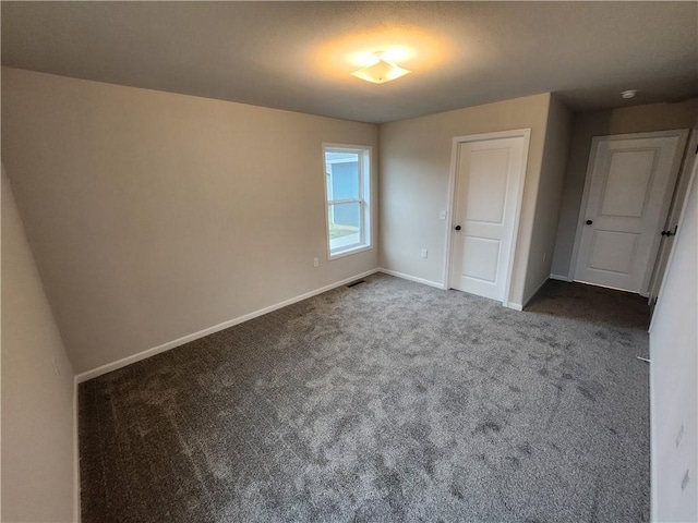 unfurnished bedroom with dark colored carpet, visible vents, and baseboards