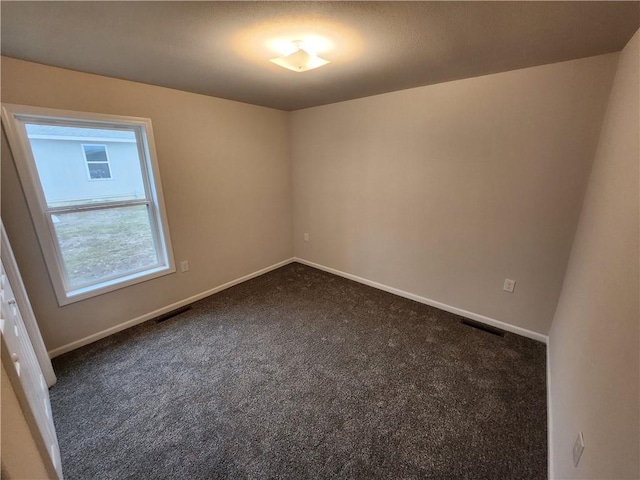 empty room featuring dark carpet, visible vents, and baseboards