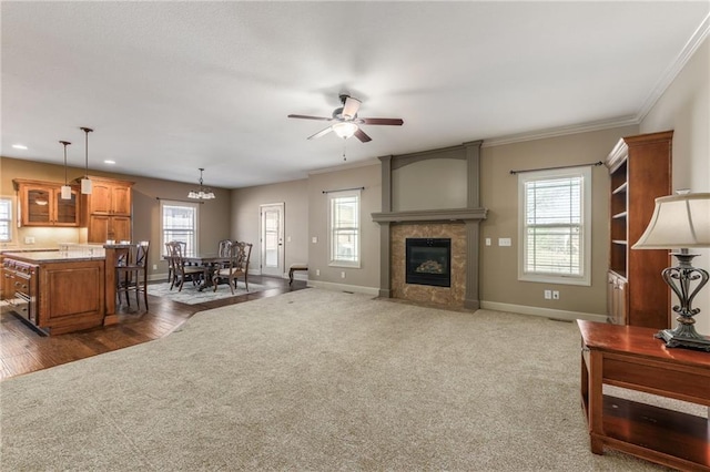 living room featuring ceiling fan with notable chandelier, baseboards, ornamental molding, and dark colored carpet