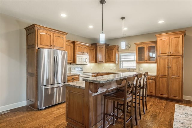 kitchen featuring decorative backsplash, white appliances, a breakfast bar, and dark wood-style floors