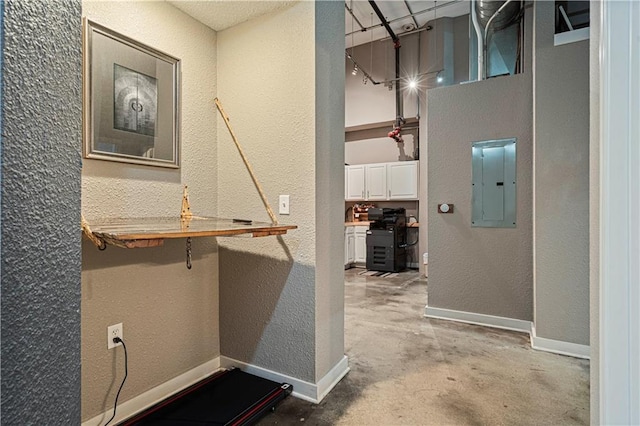 corridor with a textured wall, unfinished concrete floors, electric panel, and baseboards