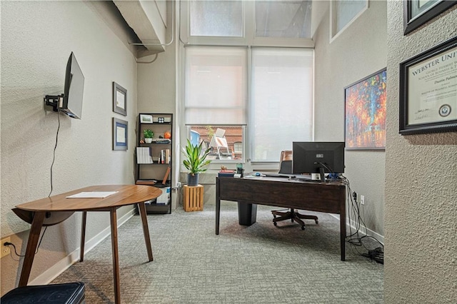 carpeted office space featuring a textured wall, a high ceiling, and baseboards