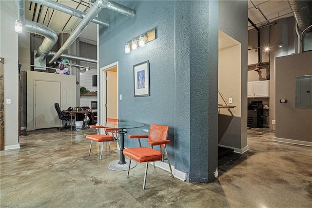 sitting room featuring a towering ceiling, electric panel, concrete floors, and baseboards