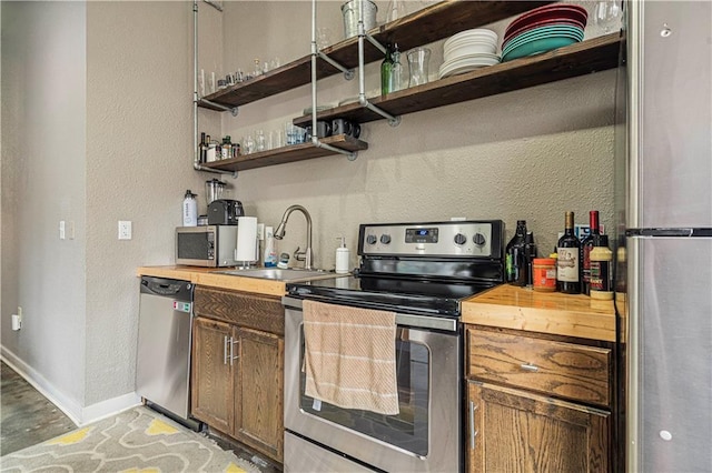 kitchen with stainless steel appliances, butcher block countertops, a sink, baseboards, and open shelves