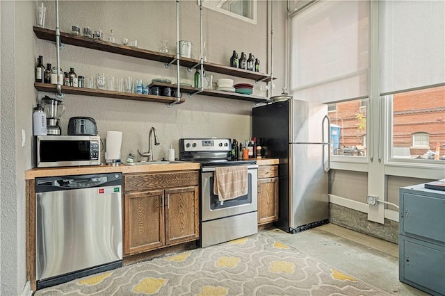 kitchen featuring brown cabinets, open shelves, stainless steel appliances, a sink, and unfinished concrete floors