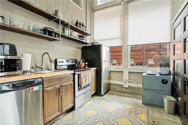 kitchen featuring unfinished concrete flooring, open shelves, light countertops, appliances with stainless steel finishes, and a sink